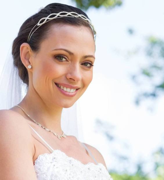 Woman smiling, holding bouquet of white roses in garden wearing wedding gown and veil, copy space. Bridal, celebration, elegance, nature, romance, sophistication, happiness